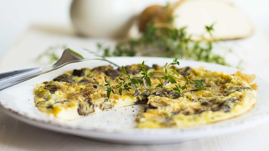 Close up of an omelette with fresh herbs on a white plate and table setting.