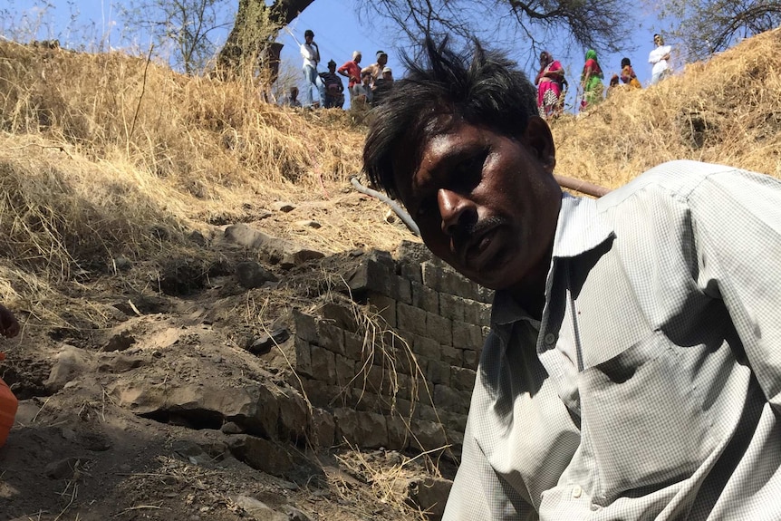 Suresh Kasbe fills pots up with murky water remaining at the bottom of wells.