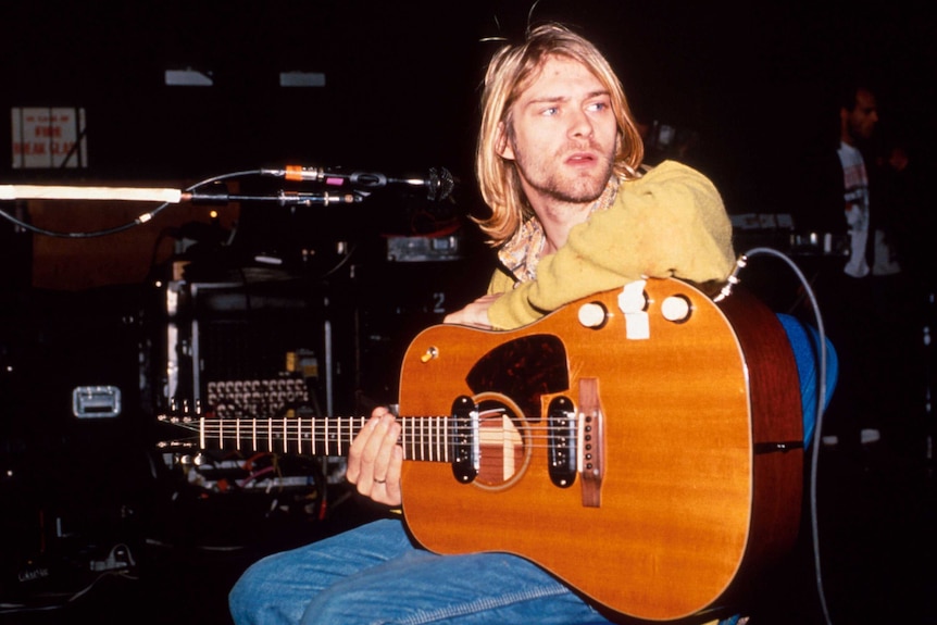 Kurt Cobain of Nirvana sits and rests a guitar on his lap.