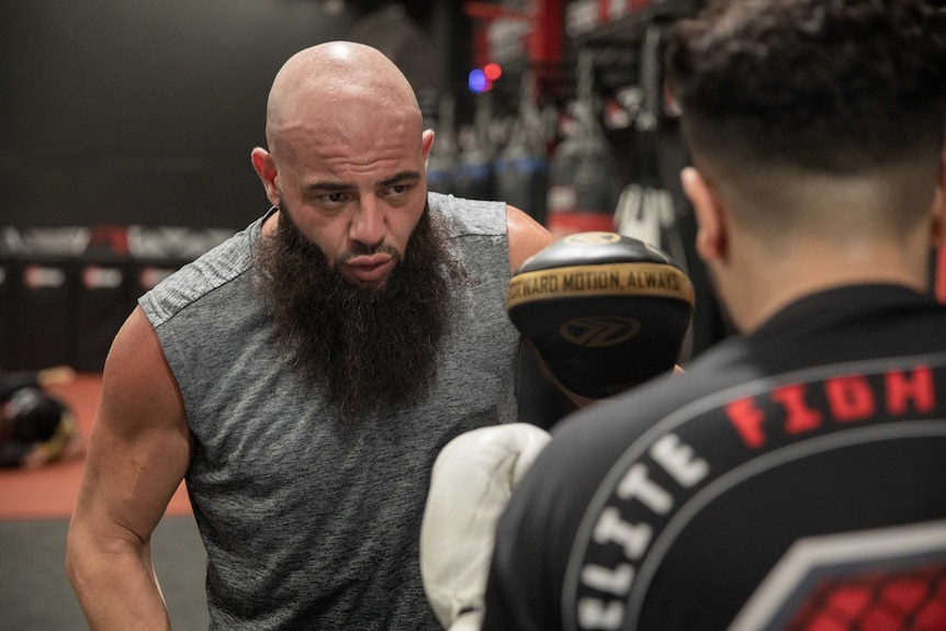 A man holds up a focus pad to while another man prepares to punch it.