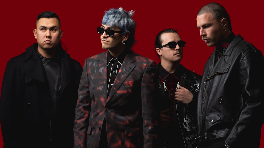Four males, two wearing dark sunglasses, all dressed in dark clothing against red background