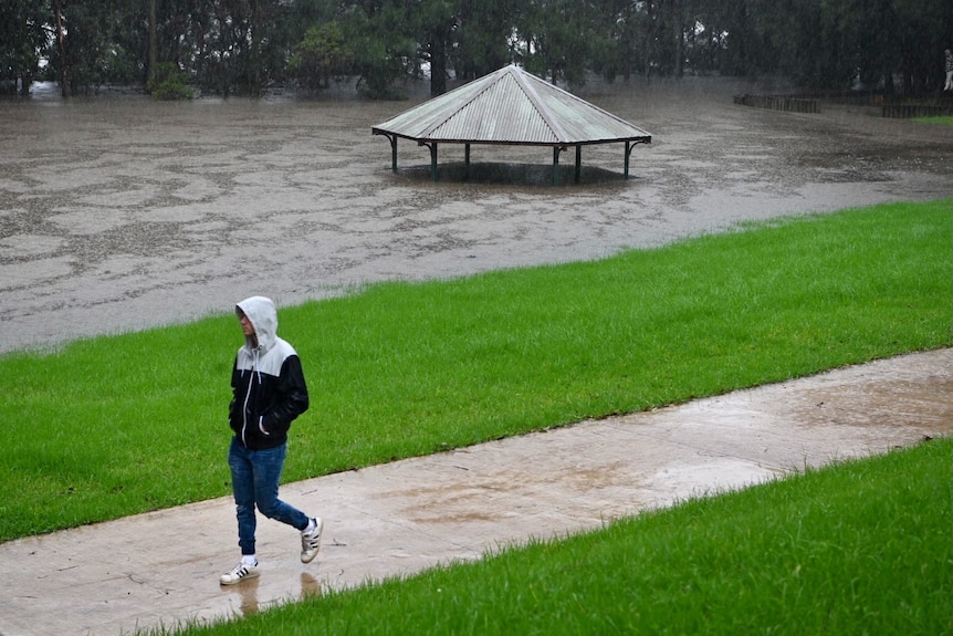 A man walking past a large amount of water, with the roof of a picnic table just visible above the water