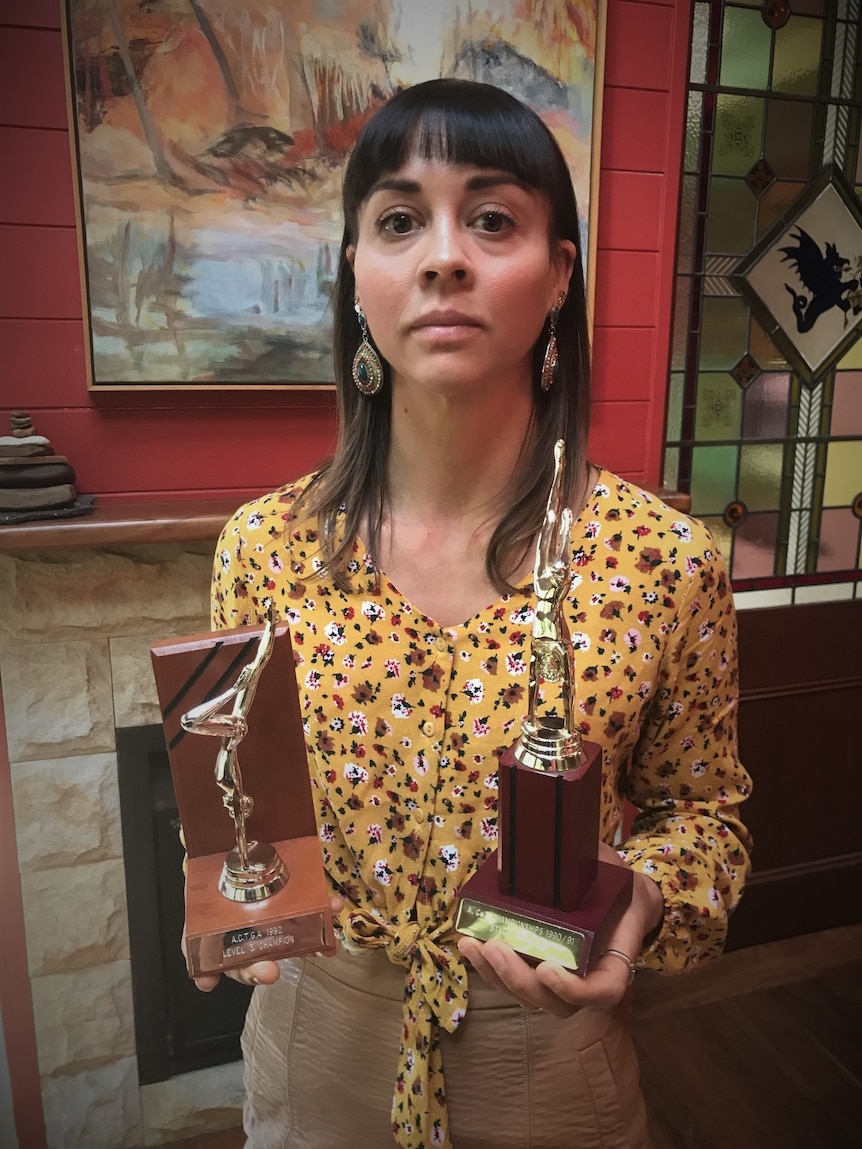 An unsmiling woman holds two trophies.