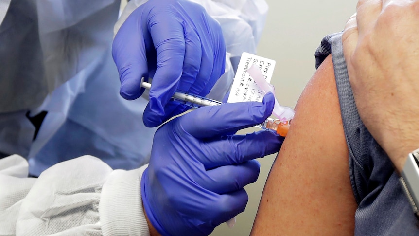 A health professional with gloves injecting in a person's arm.