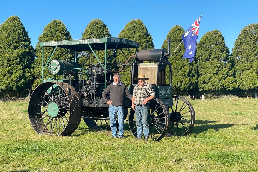 Two men standing in front of a vintage tractor