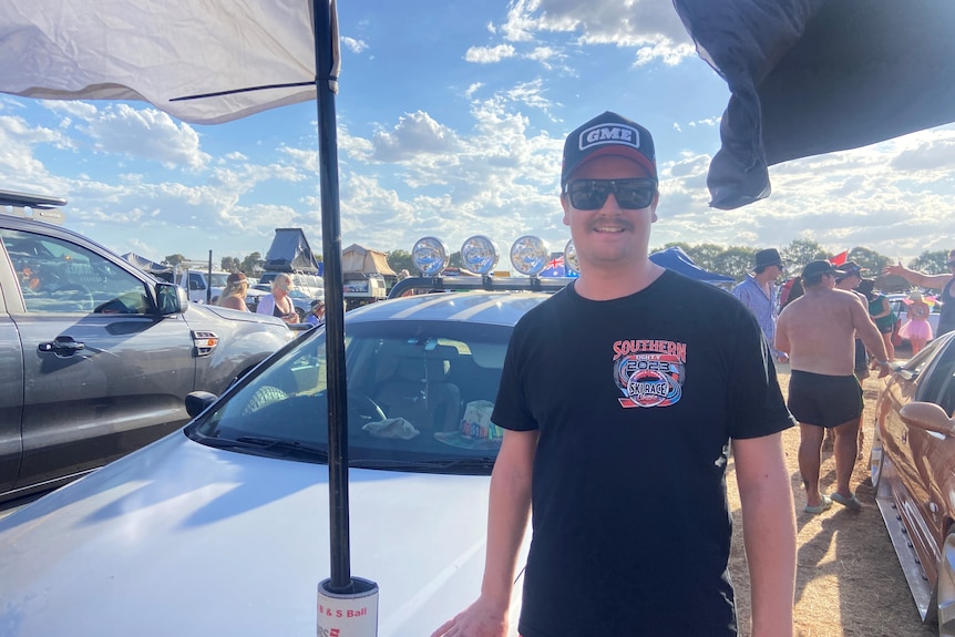 a photo of a young guy wearing southern 8p t shirt, sunnies and hat, infront of a car