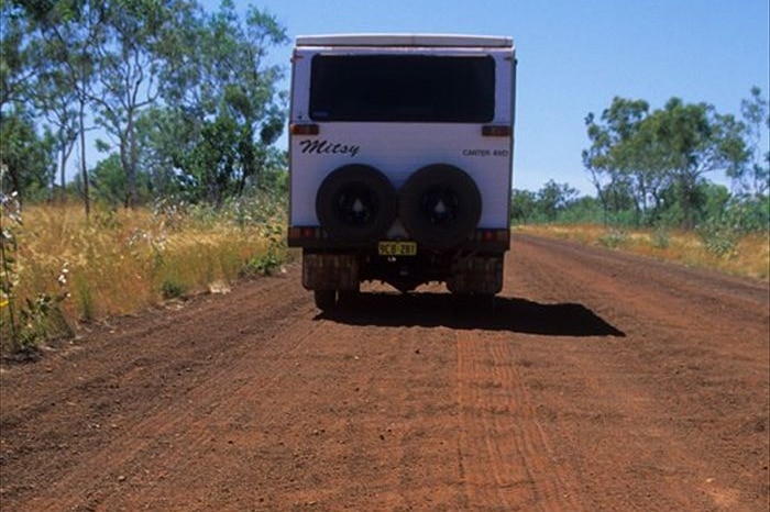 A caravan drives down a corrugated red-dirt road