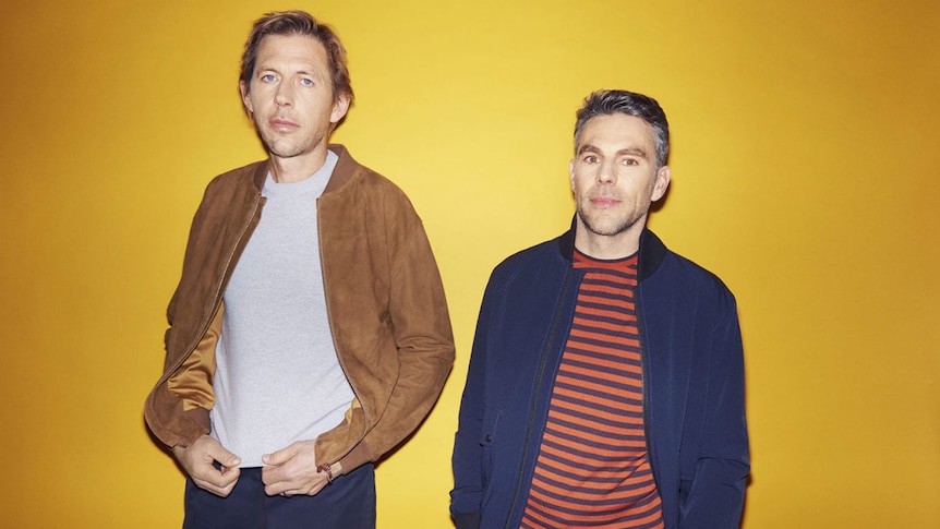 Andy and Tom of Groove Armada wearing jackets against a yellow background