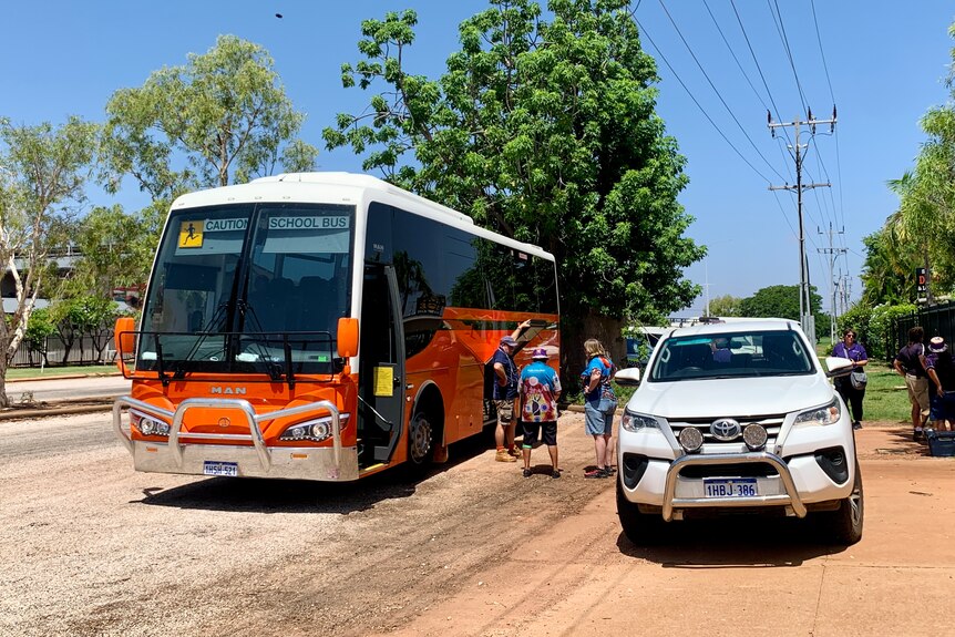 An orange bus and white four-wheel drive with some people standing between them.