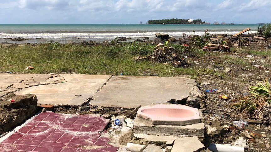 A squat toilet amid wreckage at a beachside dwelling.