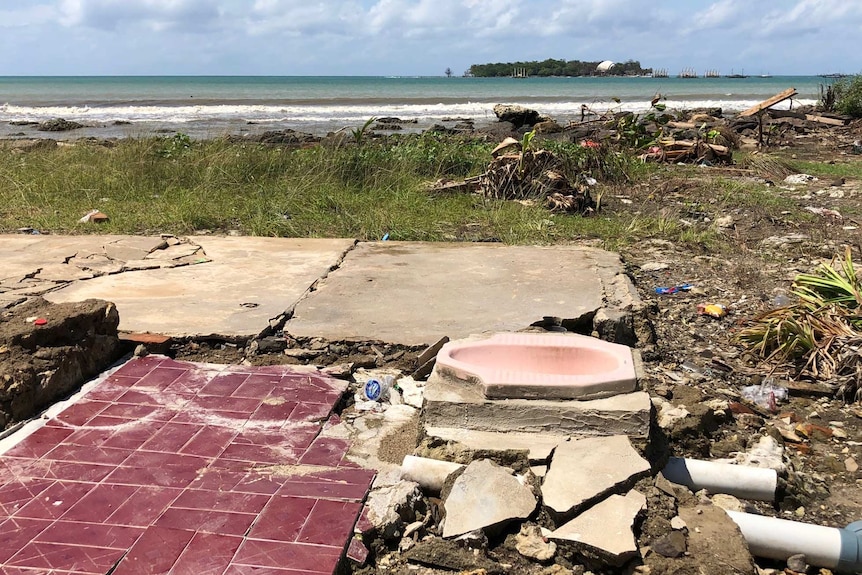 A squat toilet amid wreckage at a beachside dwelling.