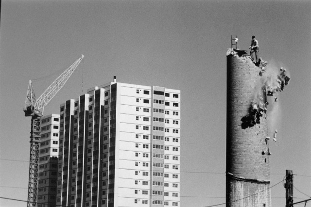 The demolition of a chimney, with the construction of housing commission flats in the background.