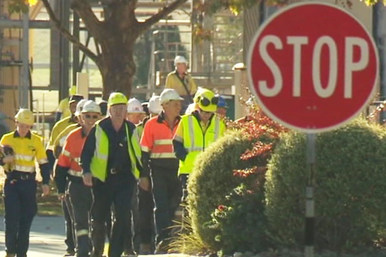 A group of workers dressed in hi-vis clothing walk together in front of industrial equipment.