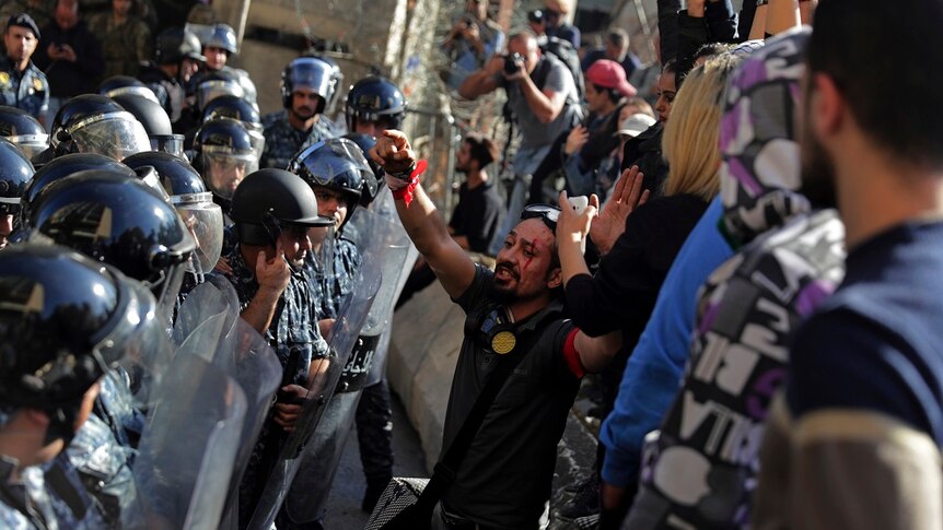 Lebanese riot policemen stand guard as protesters shout slogans after they removed barbed wire on a road.