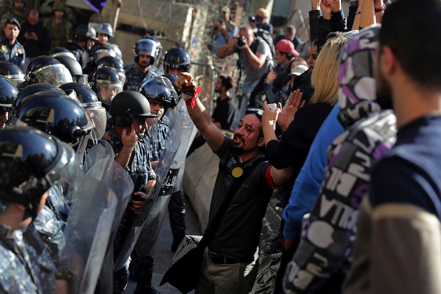 Lebanese riot policemen stand guard as protesters shout slogans after they removed barbed wire on a road.
