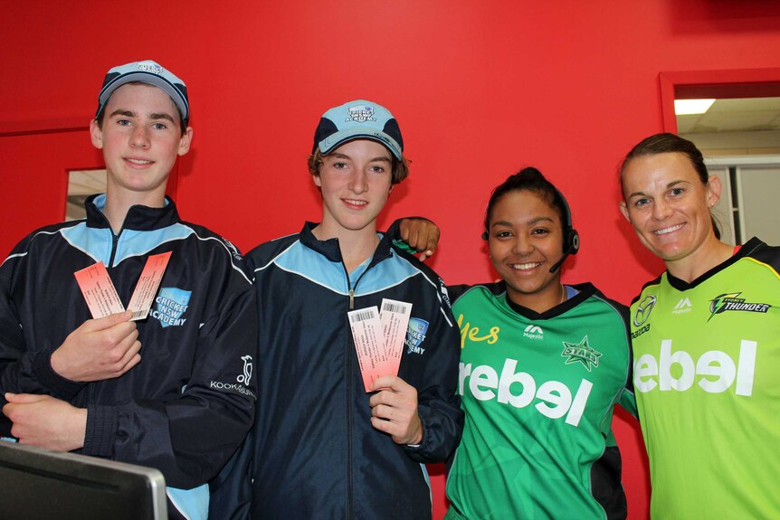 Two teengage boy stand next to two female cricketers holding tickets.