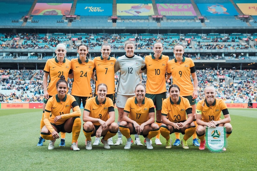 A women's soccer team wearing yellow and green poses for a photo before a game