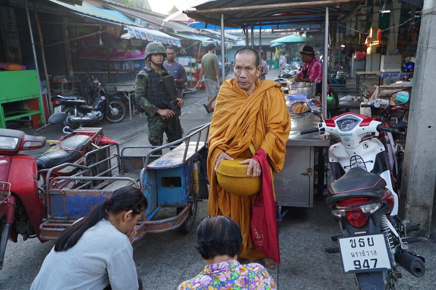 Thai soldiers watch over a Buddhist monk accepting food donations on the streets of Narathiwat.