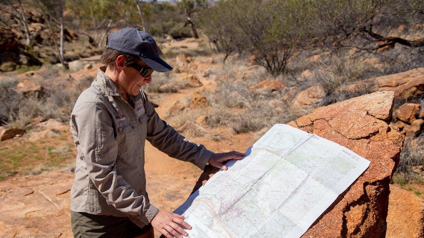 Claire Drabsch, dressed in Khaki, looks at a large format map while standing in the bush.