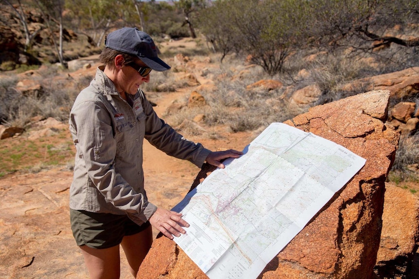 Claire Drabsch, dressed in Khaki, looks at a large format map while standing in the bush.