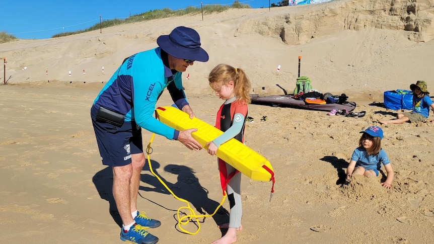 Lifeguard shows a girl how to use a rescue tube.