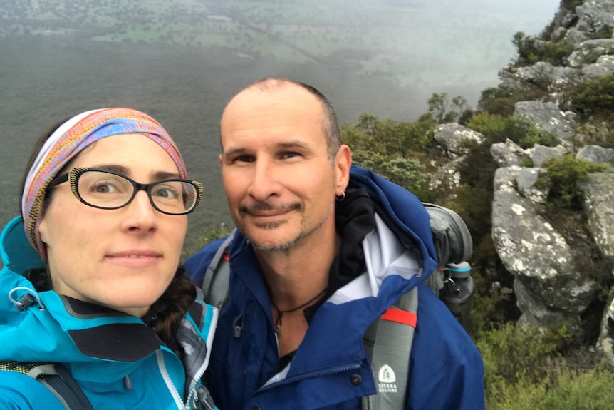 A selfie of a couple standing on top of a mountain in outdoors gear. 