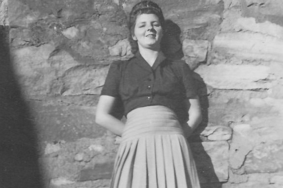 A black and white photo of a young woman standing up against a brick wall