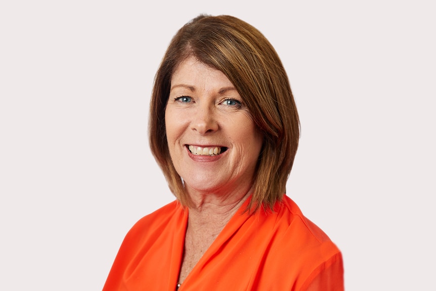 A woman in an orange shirt against a plain background.