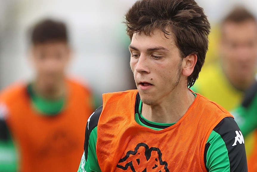 Noah Botic looks down at the ball and runs, wearing an orange bib