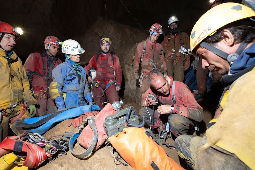 A group of people wearing safety helmets gather inside a cave talking