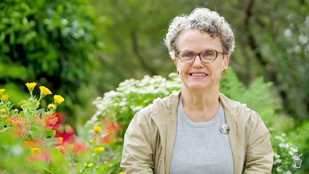 A smiling woman wearing glasses, sitting in a garden.
