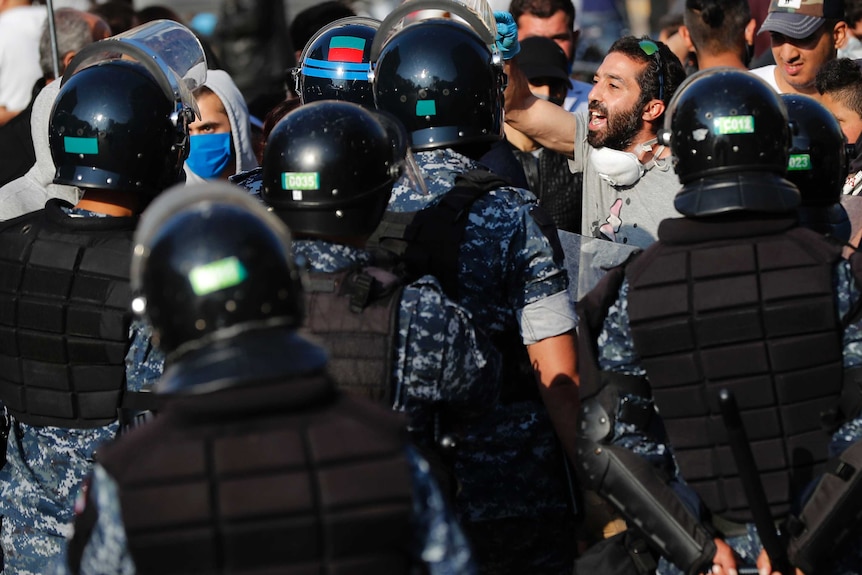 A group of police in black helmets and backs to camera confront a bearded man in T-shirt in crowd