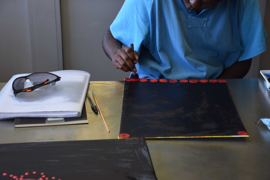 Woman using red paint on black canvas, painting dots with sponge