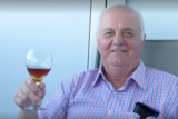 An older man with a glass of wine smiling at the camera