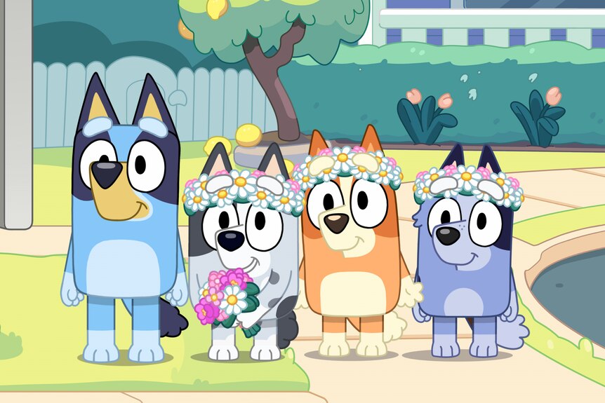 A still from Bluey showing Bluey next to Muffin, Bingo and Socks. The last three wear flower crowns