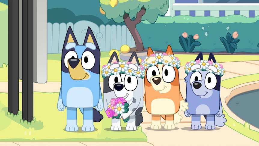 A still from Bluey showing Bluey next to Muffin, Bingo and Socks. The last three wear flower crowns