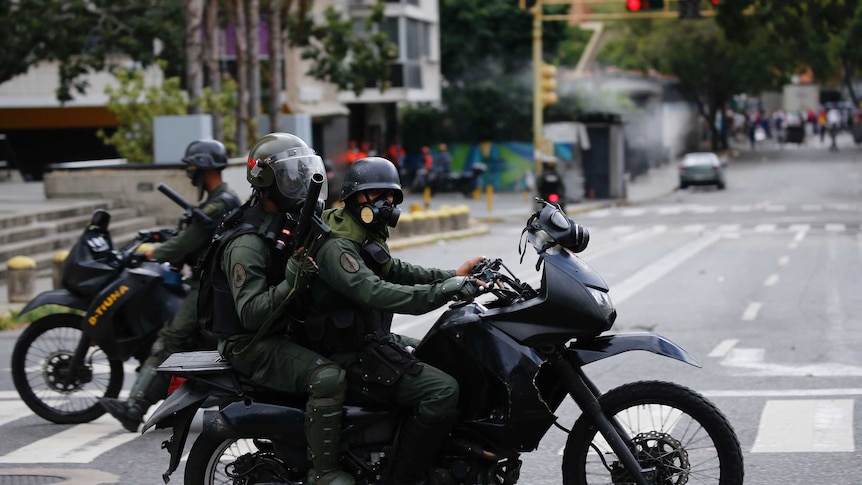 Venezuelan Bolivarian National Guardsmen look for anti-government protesters on motorbikes, they have gas masks and helmets on.