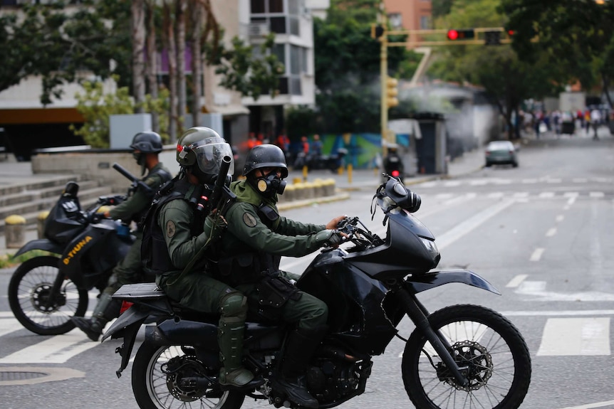 Venezuelan Bolivarian National Guardsmen look for anti-government protesters on motorbikes, they have gas masks and helmets on.