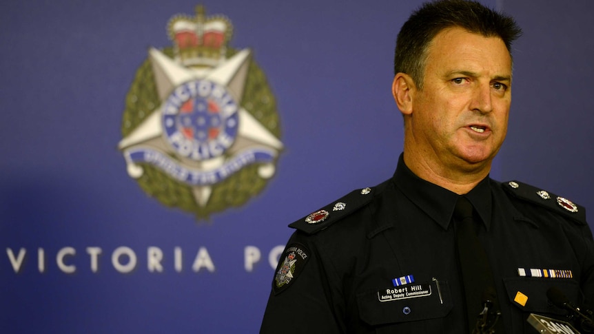 Robert Hill, dressed in a police uniform and standing in front of a Victoria Police banner, speaks at a media conference.