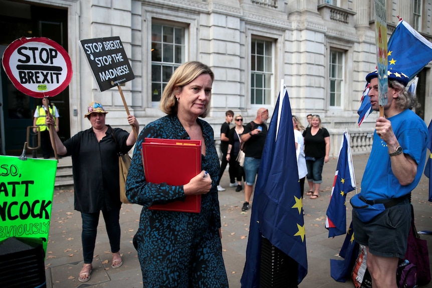 Amber Rudd walks among people with placard protesting against Brexit.
