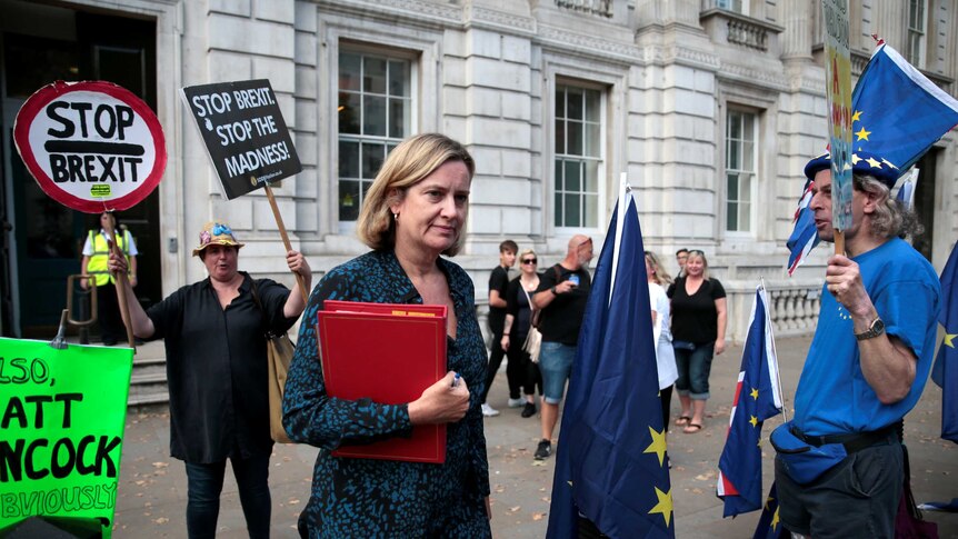 Amber Rudd walks among people with placard protesting against Brexit.