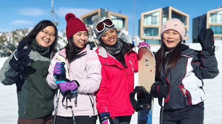 Maria Lukmanasari and three other women pose for a photo in a snowy area. They are holding skis and snowboards.
