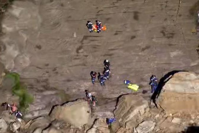 An aerial shot of emergency workers on a forbidding rock shelf.