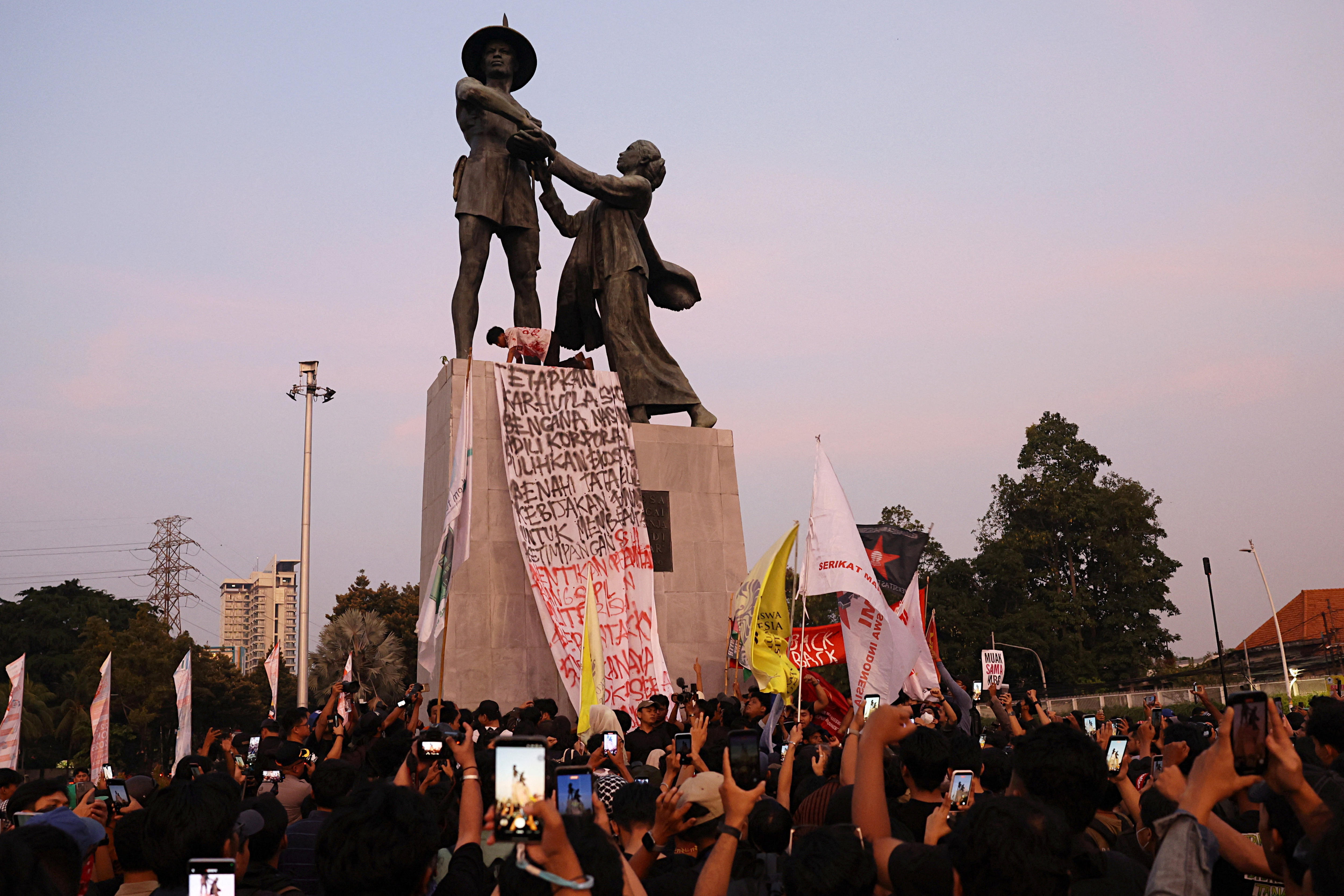 A group of people gathers under a monument holding banners and posters