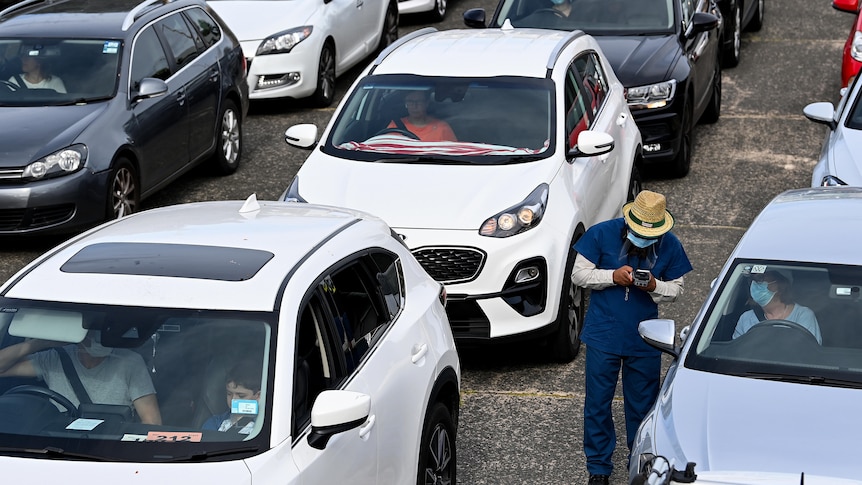 A nurse tests someone for COVID in a line of cars