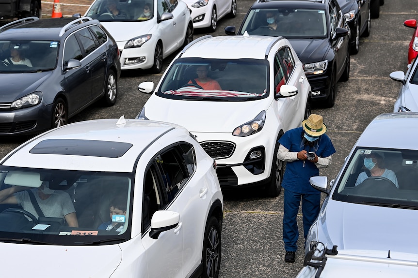 A nurse tests someone for COVID in a line of cars