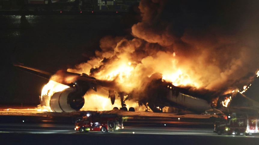 White plane engulfed in flames at night on tarmac at Haneda airport in Tokyo, Japan
