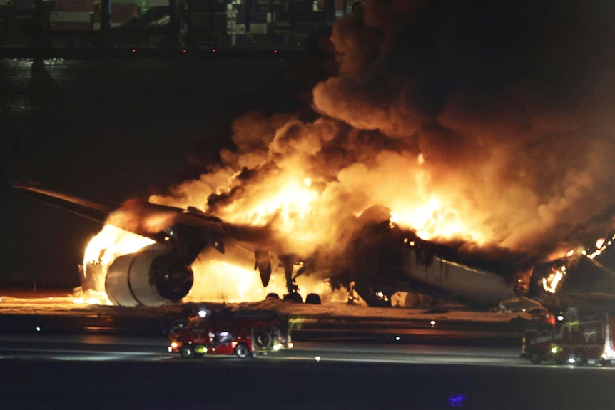 White plane engulfed in flames at night on tarmac at Haneda airport in Tokyo, Japan