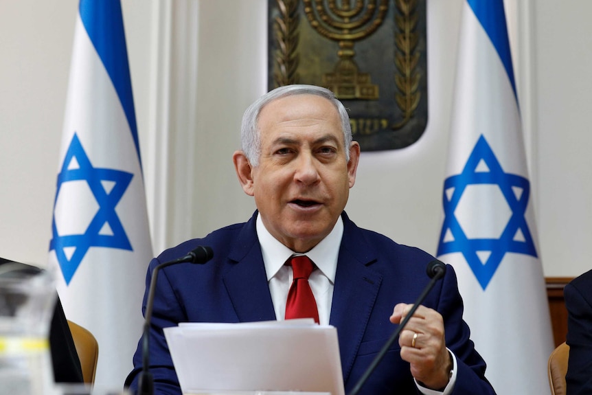 Israeli Prime Minister Benjamin Netanyahu speaking at a podium with Israeli flags in the background.