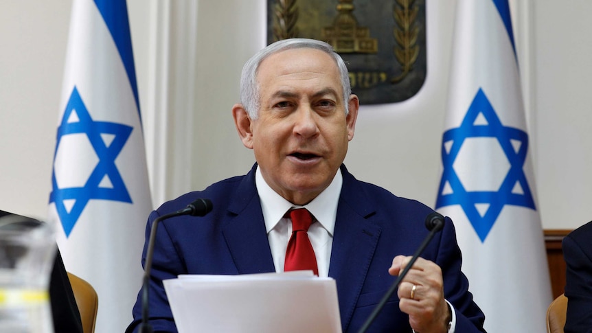 Israeli Prime Minister Benjamin Netanyahu speaking at a podium with Israeli flags in the background.